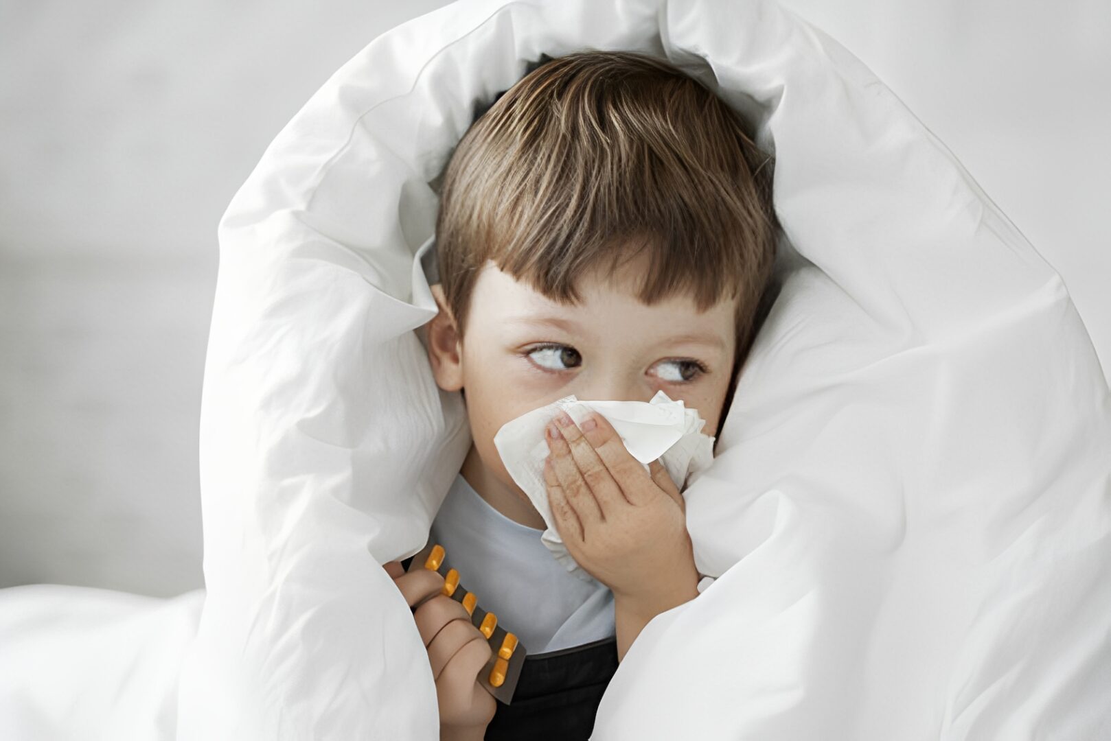 Child wrapped in blanket, holding tissues